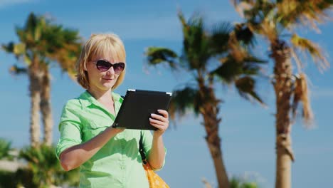 A-Woman-In-A-Light-Green-Shirt-Using-Tablet-Against-The-Sky-And-Palm-Trees