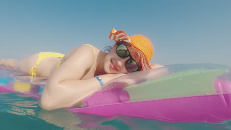 Attractive-Woman-In-An-Orange-Hat-Floats-In-The-Sea-On-An-Inflatable-Mattress