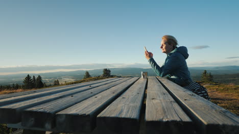 A-Woman-Sits-At-A-Table-Uses-Her-Phone-High-In-The-Mountains-Of-Norway-4k-Video