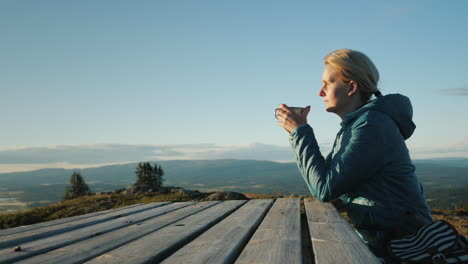 A-Woman-Traveler-Sits-At-A-Table-High-In-The-Mountains-Drinking-Tea-Far-From-Civilization-Nature-Of-