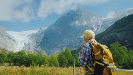 An-Active-Woman-With-A-Backpack-Walks-Against-The-Backdrop-Of-The-Mountains-And-The-Briksdal-Glacier