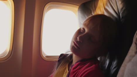 The-Little-Girl-Is-Sleeping-In-The-Cabin-Of-The-Plane-During-The-Dawn-The-Orange-Rays-Of-The-Sun-Ill