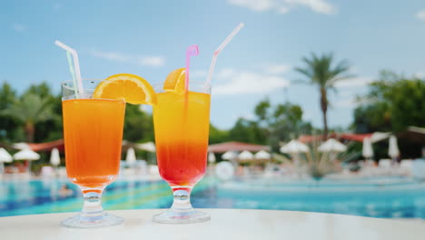 Entspannen-Sie-Auf-Den-Sonnenliegen-Am-Pool-Mit-Zwei-Exotischen-Cocktails-Mit-Strohhalmen-Blauer-Himmel-Und-Grüner-Pal