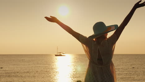 A-Young-Woman-Enjoys-The-Sunrise-Over-The-Sea-Emotionally-Waving-Her-Hands-A-Ship-Is-Visible-In-The-