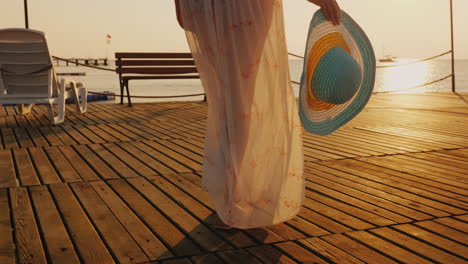 A-Woman-Walks-The-Pier-Towards-The-Rising-Sun-In-The-Picture-You-Can-See-A-Hand-With-A-Hat-Travel-An
