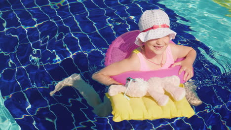 A-Little-Girl-Is-Playing-With-A-Toy-Rabbit-In-The-Pool-The-Hare-Is-Floating-On-An-Inflatable-Mattres