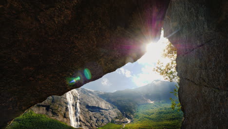 Die-Sonne-Scheint-Durch-Ein-Loch-Im-Felsen,-Wo-Man-Berge-Mit-Einem-Wasserfall-Und-Einem-Bild-Sehen-Kann