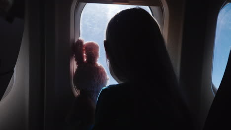 The-Child-Together-With-The-Toy-Hare-Looks-Through-The-Airplane-Window-Vacation-With-A-Child-And-Tra