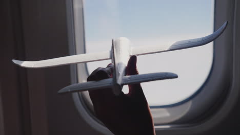 A-Child's-Hand-Holds-A-Toy-Airplane-Against-The-Background-Of-The-Airplane-Window-Dreams-And-Travel-