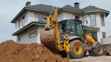 Excavator-Digs-A-Hole-For-Laying-Communications-Against-The-Background-Of-A-Modern-Two-Story-House