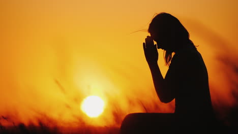 Silhouette-Of-A-Woman-Praying-Against-The-Background-Of-An-Orange-Sky-And-A-Large-Setting-Sun