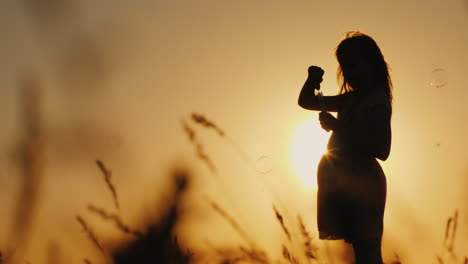 Silhouette-Of-A-Girl-Playing-With-Soap-Bubbles-In-The-Tall-Grass-At-Sunset