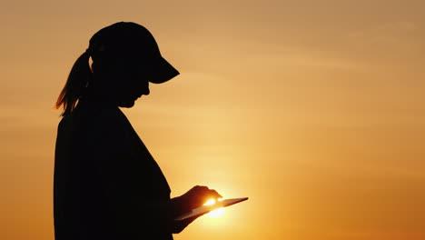 Silhouette-Of-A-Woman-Farmer-Working-With-A-Tablet-At-Sunset-Side-View