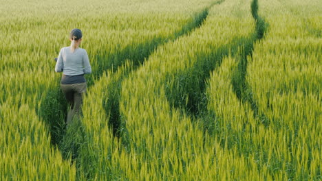 Young-Woman-Farmer-Walking-In-A-Field-Of-Green-Wheat