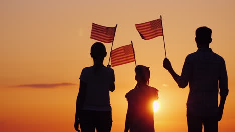 Happy-Family-With-Child-Waving-Us-Flags-At-Sunset-Rear-View