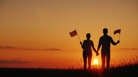 A-Young-Couple-With-The-Flags-Of-The-United-States-In-Their-Hands-Admires-The-Beautiful-Sunset-Indep
