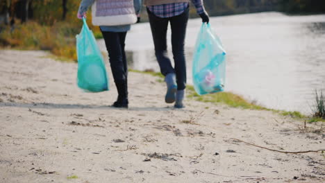 Woman-Volunteer-With-A-Child-Walk-Along-The-Lake-Carry-Packages-With-Garbage