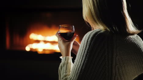 Woman-Drinking-Red-Wine-While-Sitting-By-The-Fireplace-Rear-View