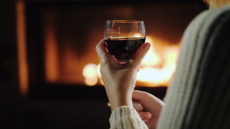 Female-Hand-With-A-Glass-Of-Red-Wine-On-A-Background-Of-Flame-In-A-Fireplace