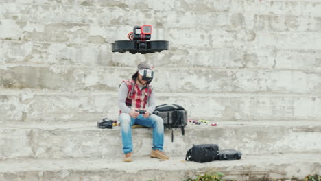 Ein-Mann-In-Einem-Helm-Mit-Telemetrie-Steuert-Eine-Drohne,-Die-Vor-Ihm-Fliegt