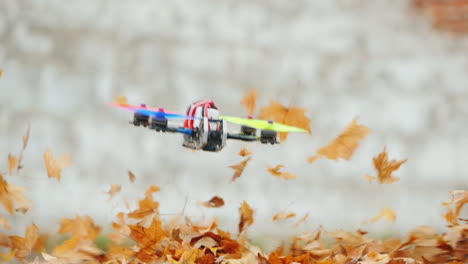 Masterly-Piloting-A-Movie-Drone-Flying-Low-Above-The-Ground-Dry-Leaves-Fly-Away-From-The-Wind-Slow-M