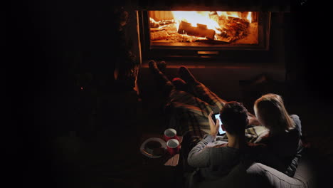 Man-And-Woman-Use-A-Tablet-In-Their-Living-Room-Near-The-Fireplace-Top-View