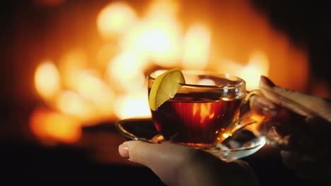 Woman's-Hands-With-A-Cup-Sat-By-The-Fireplace-Keep-Warm-In-Winter-Concept