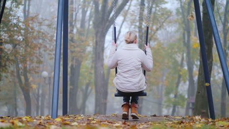 Rear-View-Of-A-Woman-Sitting-On-A-Swing-In-A-Park-Where-There-Is-Heavy-Fog-Loneliness-Concept