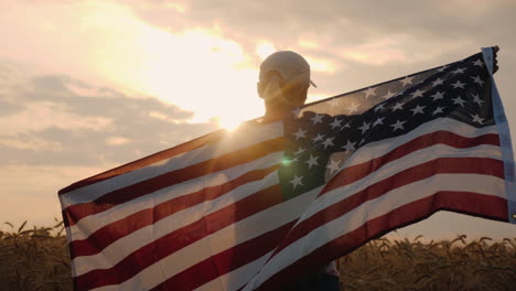 Middle-Aged-Woman-With-Usa-Flag-Stands-In-A-Wheat-Field-At-Sunset-Independence-Day-Concept