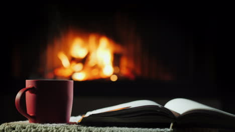 An-Open-Book-And-A-Cup-Of-Hot-Tea-On-The-Background-Of-The-Fireplace-Where-The-Fire-Is-Burning