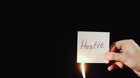 Hand-Holds-Burning-Paper-With-Inscription-Health