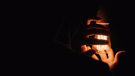 Back-View-Of-Man-Warming-His-Hands-Near-A-Luz-Bulb-In-The-Dark