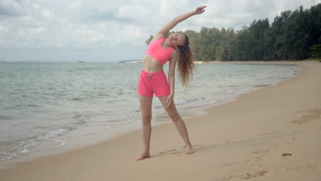 Active-woman-in-pink-swimsuit-making-workout-on-beach