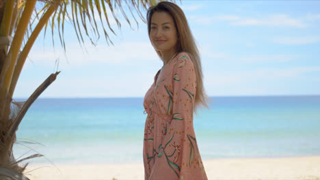 Cheerful-female-standing-near-palm-on-beach