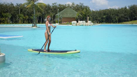 Woman-floating-on-paddle-board-in-large-swimming-pool
