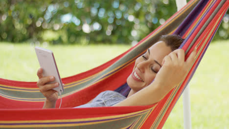 Happy-young-woman-listening-to-music-in-a-hammock