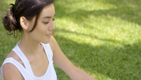 Serene-young-woman-meditating-on-a-green-lawn