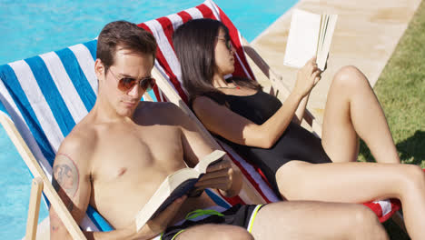 Relaxed-attractive-young-couple-reading-poolside