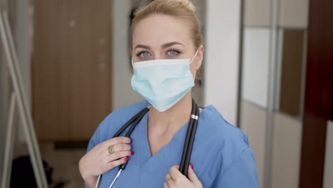 Portrait-of-young-female-doctor-in-medical-mask--blue-coat-and-stethoscope