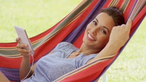 Happy-young-woman-listening-to-music-in-a-hammock