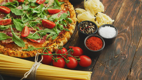 Italian-food-background-with-pizza--raw-pasta-and-vegetables-on-wooden-table
