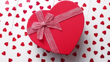 Boxed-gift-placed-on-heart-shaped-red-sequins-on-white-wooden-table