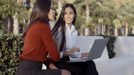 Two-pretty-women-sharing-a-laptop-outdoors