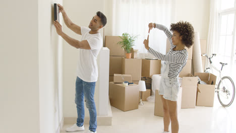 Young-couple-hanging-pictures-in-their-new-home