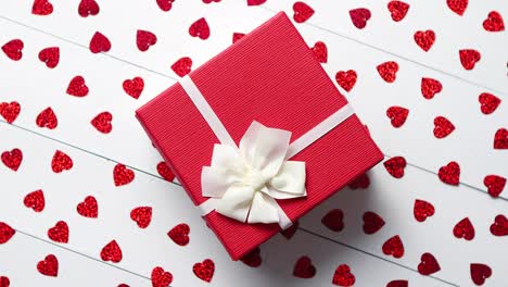 Boxed-gift-placed-on-heart-shaped-red-sequins-on-white-wooden-table