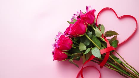 Mixed-flowers-bouquet-with-roses-and-heart-shaped-bow-on-pink-background