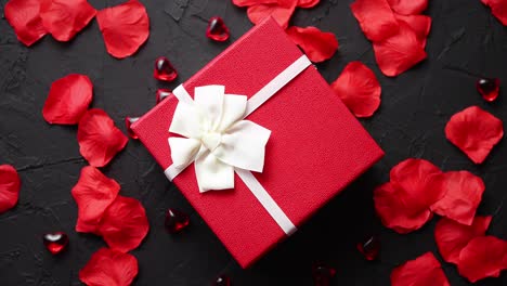 Gift-box-on-black-stone-table--Romantic-holiday-background-with-rose-petals