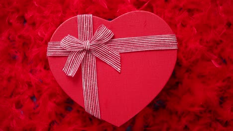 Heart-shaped-boxed-gift--placed-on-red-feathers-background