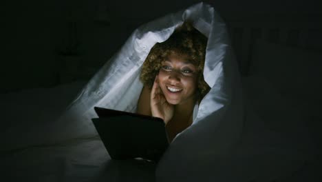 Woman-using-tablet-under-blanket
