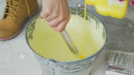 Hand-mixing-yellow-wall-paint-in-bucket-